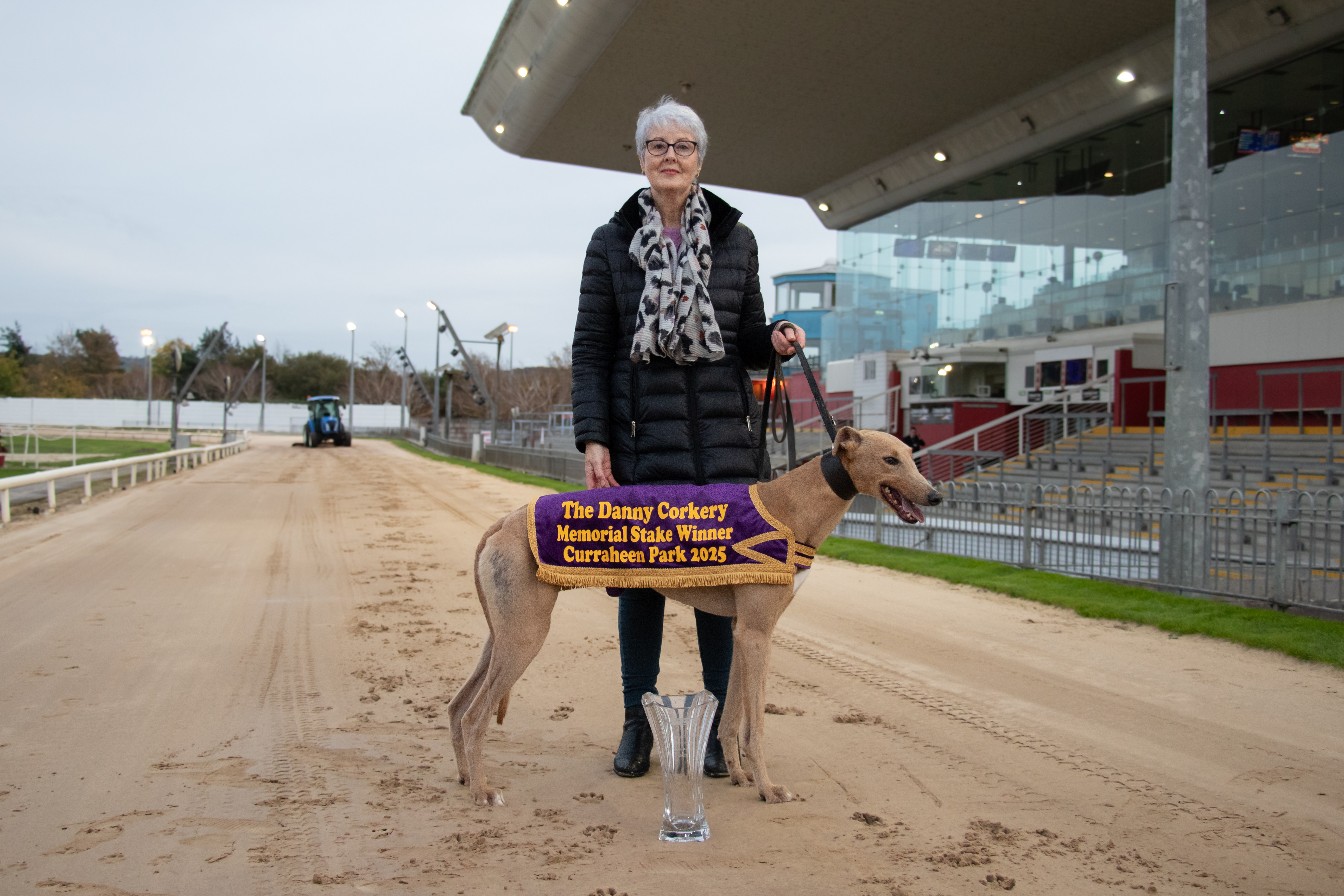 Ellen Corkery pictured at Curraheen Park Greyhound Stadium during the launch of the Danny Corkery Memorial Stake 2025. She stands trackside with the greyhound wearing the winner’s presentation jacket and trophy placed in front, celebrating the new event in honour of her late husband.