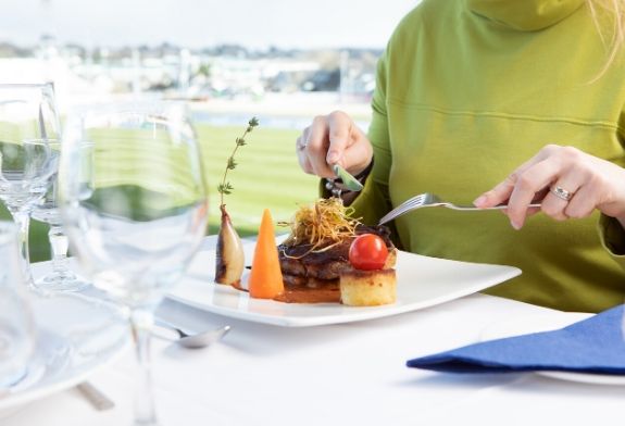 image is of a table in shelbourne park greyhound stadium restaurant fully set with cutlery, glasses and menu. Looking out onto the racing track